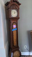 Full view of the grandfather style clock showing carved wood details and overall shape.