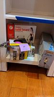 Side view of shelf showing Bally Pilates Twist Board box and boxes for Medicine Ball and Danskin Abs Rower Plus