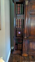 Tall wooden shelf containing multiple faux book boxes stacked vertically with realistic leather-style spines in various colors and sizes.