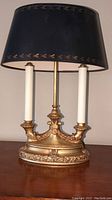 Gilded base lamp with candle-style lights and black shade with gold leaf border showing wear.