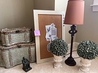 Full view of all items including the cork board, two storage baskets, the metal lamp with pink shade, two faux greens in urn pots, and Abe Lincoln sculpture.