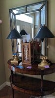 Photo showing two gold-tone base lamps with black conical shades and wood look umbrella stand on a wooden table in front of a mirror.