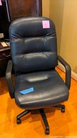 Front view of the black leather office chair showing padded backrest, seat, and armrests on hardwood floor.