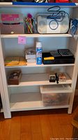 Full view of white shelving unit with various office supplies and radio on shelves