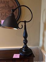 Photo of painted metal desk lamp with a curved arm, dark finish, cone shade, on wooden surface.