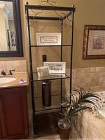 Full view of black metal shelf unit with glass and metal shelves near bathroom vanity and plant.