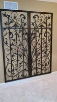 Full front view of the two matching metal wall hangings with floral scroll design side by side on a wall.