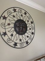 Metal sun sculpture wall hanging with central face and star design on a wall.