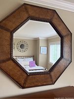 Photo of octagonal metal framed wall mirror hanging on a wall with beige room reflected in the glass.