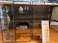 Front view of the black metal wire wall rack with three wire baskets and a hanging pot, alongside the packaged wood rack.
