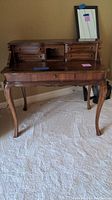 Front view of wooden writing desk showing multiple drawers, decorative carved legs, and raised back section with open compartment.