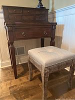 Wood desk shown with six small drawers in upper section, fold-out writing surface partly visible, larger bottom drawer with ring pull handles, and four legs with modest decorative features.