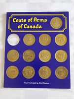 Full view of blue cardboard display board with 15 coin slots labeled 'Coats of Arms of Canada', 14 coins present with detailed coats of arms engravings