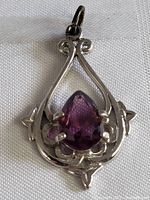 Front view of silver ornate pendant featuring a deep purple faceted pear-shaped amethyst stone.