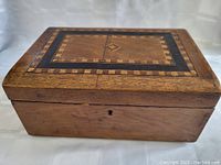 Angled view of antique wooden box showing wooden grain, aged patina, scattered wear, and front keyhole detail