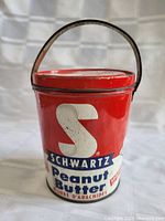 Red antique tin sand pail resembling a Schwartz Peanut Butter can with lithographed logo and text, metal handle and lid.