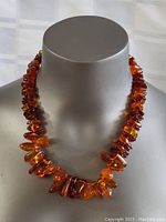 Front view of large amber bead necklace displayed on a grey mannequin bust.