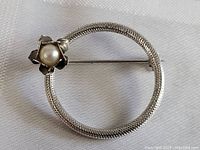 Front view showing circular textured silver brooch with central pearl in flower mount.