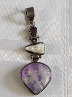 Full view of sterling silver pendant showing amethyst, pearl, and large purple heart-shaped stone connected in hinged segments with a bail on top.