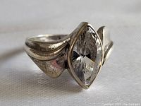 Close-up front view of sterling silver ring showing marquise-cut clear stone held by bezel setting with sculptural band.