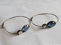 Pair of sterling silver earrings with blue oval and clear round stones on white cloth.