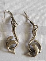 Pair of vintage sterling silver earrings featuring dolphin motif on hook style ear wires. Displayed on white textured fabric.