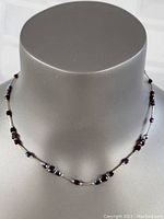 Front view of garnet necklace displayed on grey jewelry stand, showing the overall design of garnet beads and silver tube links.