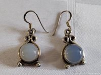 Pair of silver moonstone earrings laid side by side showing both front faces on white cloth background.