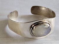 Front angled view of wide sterling silver cuff bracelet with large oval rainbow moonstone center stone, showing polished band and stone framing.