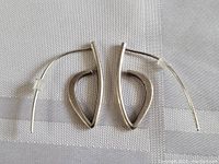Pair of sterling silver earrings with open geometric punk style design showing front and side angles on a textured light background.