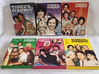 Photo of six DVD box sets for Three's Company seasons 1 to 6 with colorful front packaging showing main cast members.