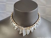 Front view of the vintage conch shell leaf necklace displayed on a mannequin bust, showing the carved leaves, pearl closure, and pink sequin details.