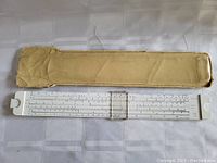 White plastic slide rule with clear cursor laid out flat showing measurement scales and numbers.