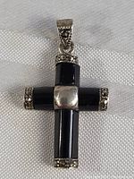 Front view of the vintage sterling silver onyx cross pendant lying on a light fabric, showing polished black onyx arms, silver center piece, and marcasite details on ends and bail.