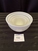 Four white vintage nesting Fire King bowls stacked inside each other on a black surface.