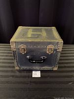 Closed antique black metal case showing brass corner protectors, handle, and clasps.