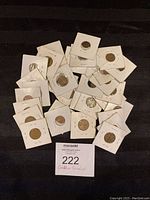 Top view of assorted Canadian coins individually housed in white paper holders, scattered on a black cloth background with a lot label.