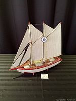 Front and side view of the wooden ship model showing three white sails, rigging, and wooden hull