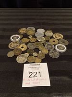 Top view of mixed coins and tokens spread out, showing different shapes and sizes including square-holed tokens and commemorative coins