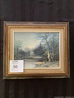 Full view of the framed original landscape painting depicting a river and trees with visible artist signature and frame.