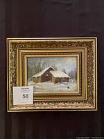 Full view of framed oil painting showing snow-covered wooden cabin in winter landscape.