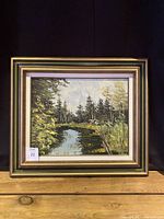 Frontal photo of the framed oil painting showing a forest landscape with a river, signed and with a lot tag.