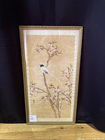 Full view of the framed painting showing bird on blossoming tree branch against beige background.