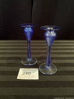 Front view of pair of cobalt blue art glass candle holders with twisted stems and clear bases on a black and brown striped surface.