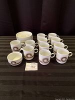 10 Rosenthal Studio-Line mugs, 10 matching saucers, 1 sugar bowl, 1 creamer arranged on table with black cloth background