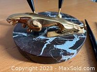 Close-up of bronze jaguar figure on marble base, showing shape, material and holder attachment point.