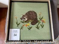 Full view of framed embroidered raccoon artwork showing the raccoon amongst flowers with fabric background and original frame.