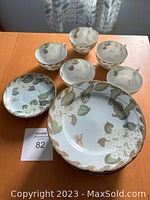 Overview photo showing 6 porcelain pieces: teacups and plates with handpainted green leaves, white hydrangea flowers, and butterflies.