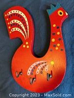 Front view of the bright red wooden bird keyholder with colorful stencilled details and three metal hooks on the body.