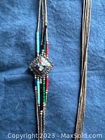 Full view of five strand sterling silver liquid silver necklace with offset square pendant featuring inlaid turquoise, lapis, malachite, red coral, and onyx beads.